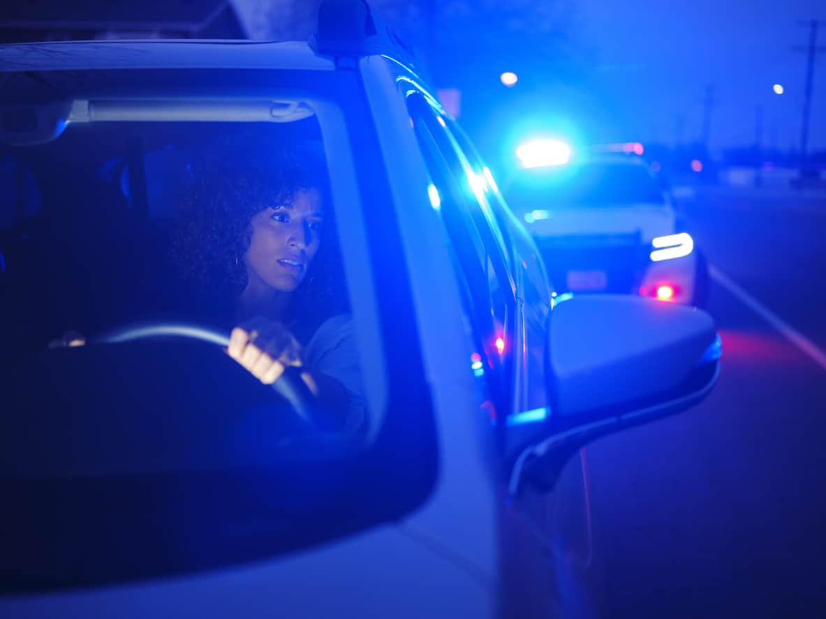 A young woman in a car, pulled over by a police officer at night for DUI.