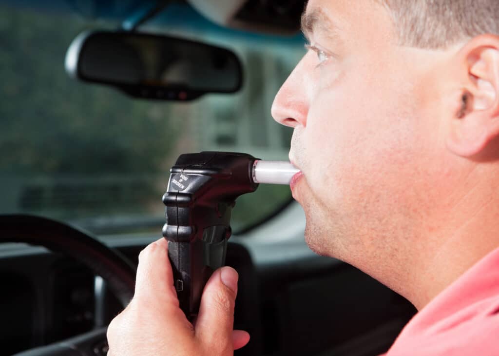 A male driver is blowing into an ignition interlock system which checks his alcohol concentration before allowing the vehicle to be started. Ignition interlock devices may be an alternative sentence for drunk driving or a probation requirement for those who have received a DUI.